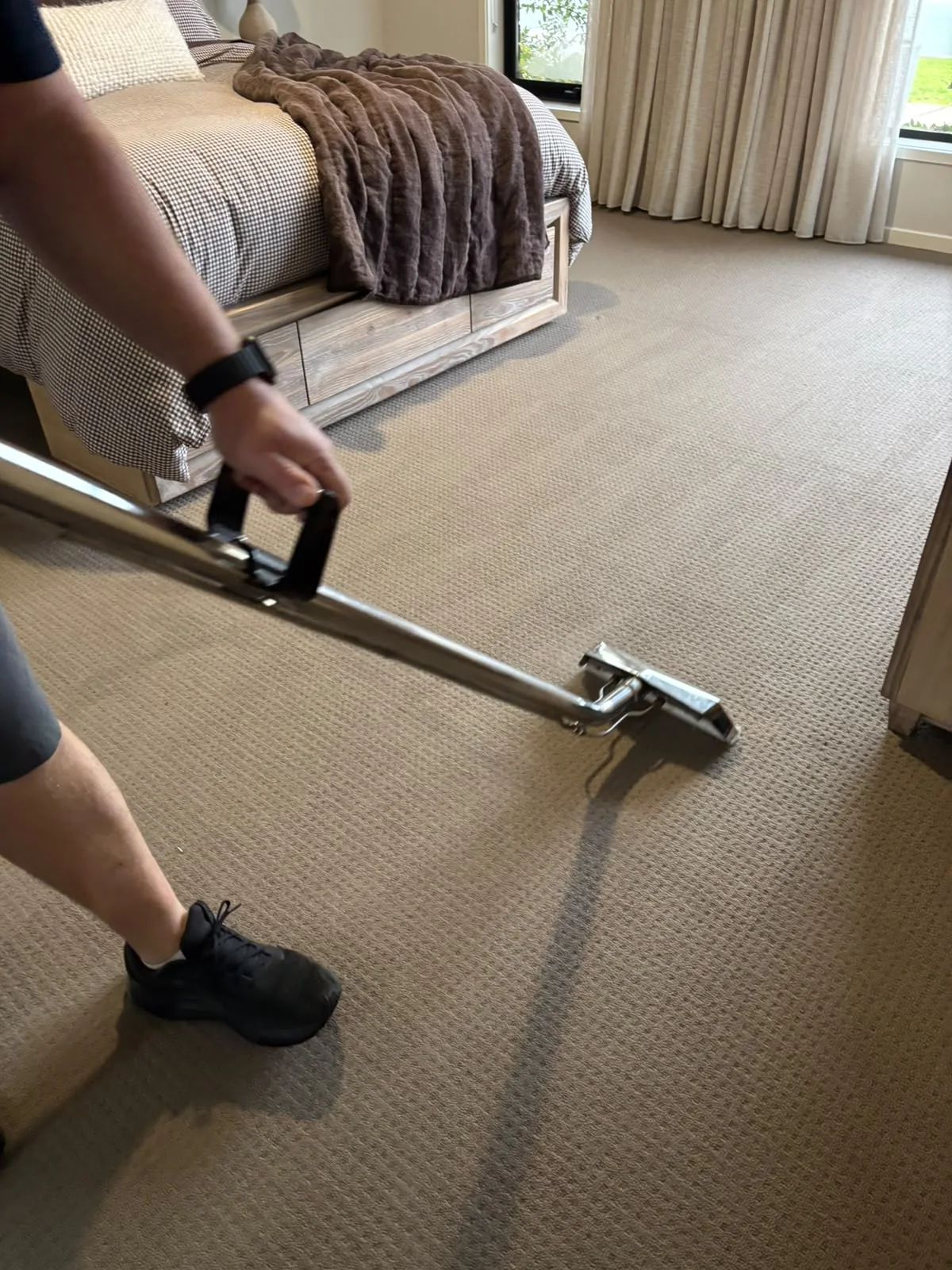 Carpet cleaner using a stainless steel extraction wand across a bedroom carpet