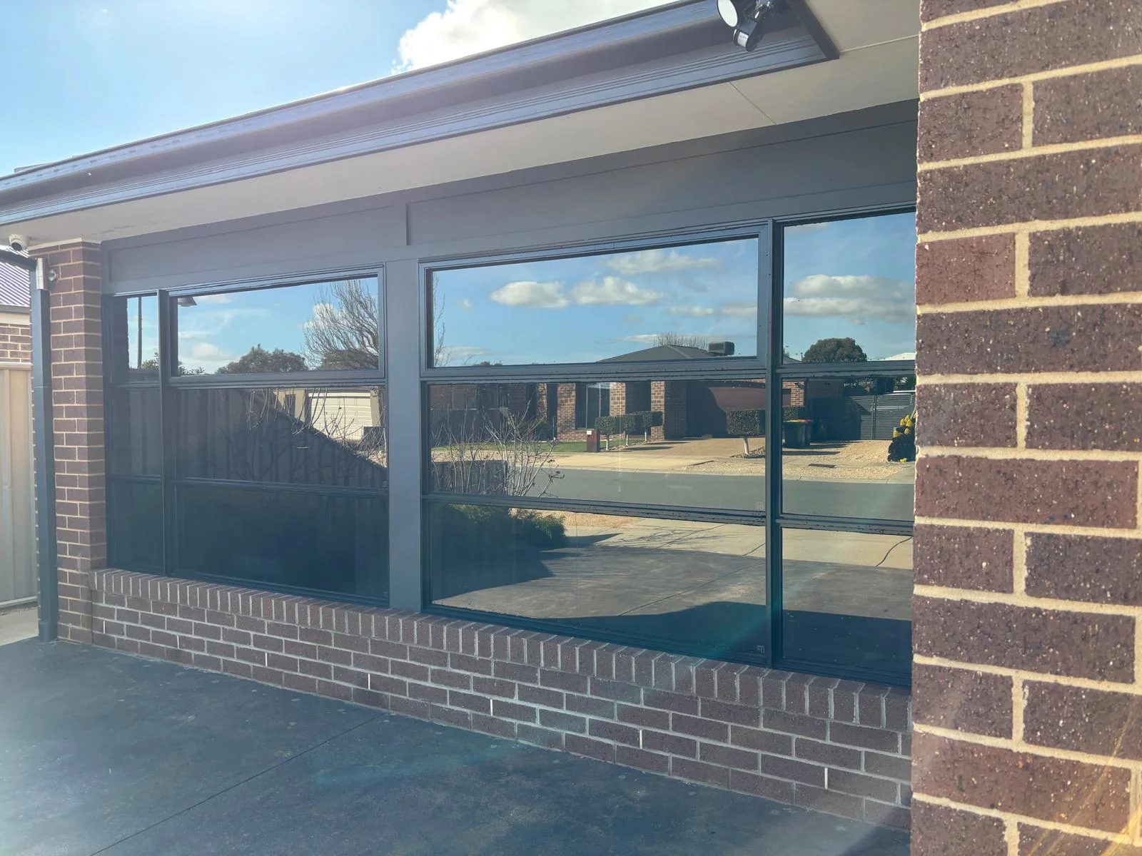 Clean dark-framed residential windows reflecting blue sky and nearby homes