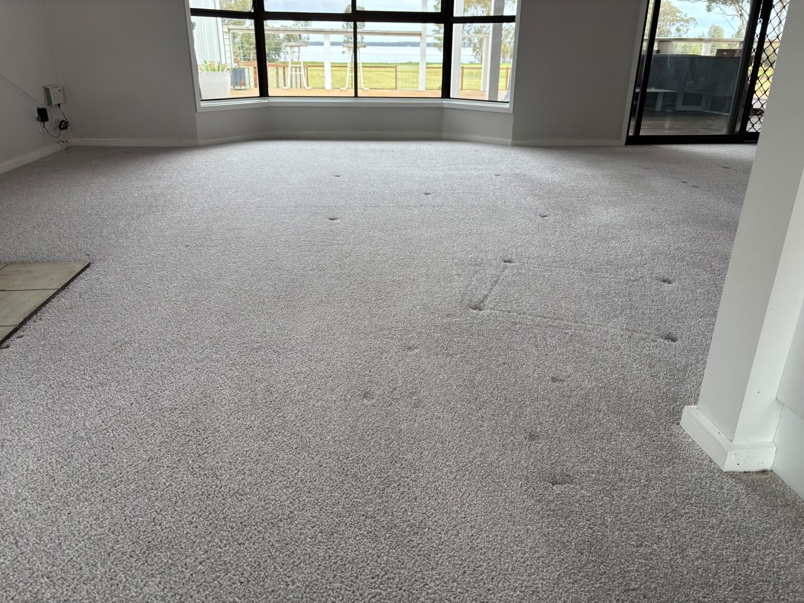 Wide view of grey carpet across an empty lounge room with bay windows and a sliding door
