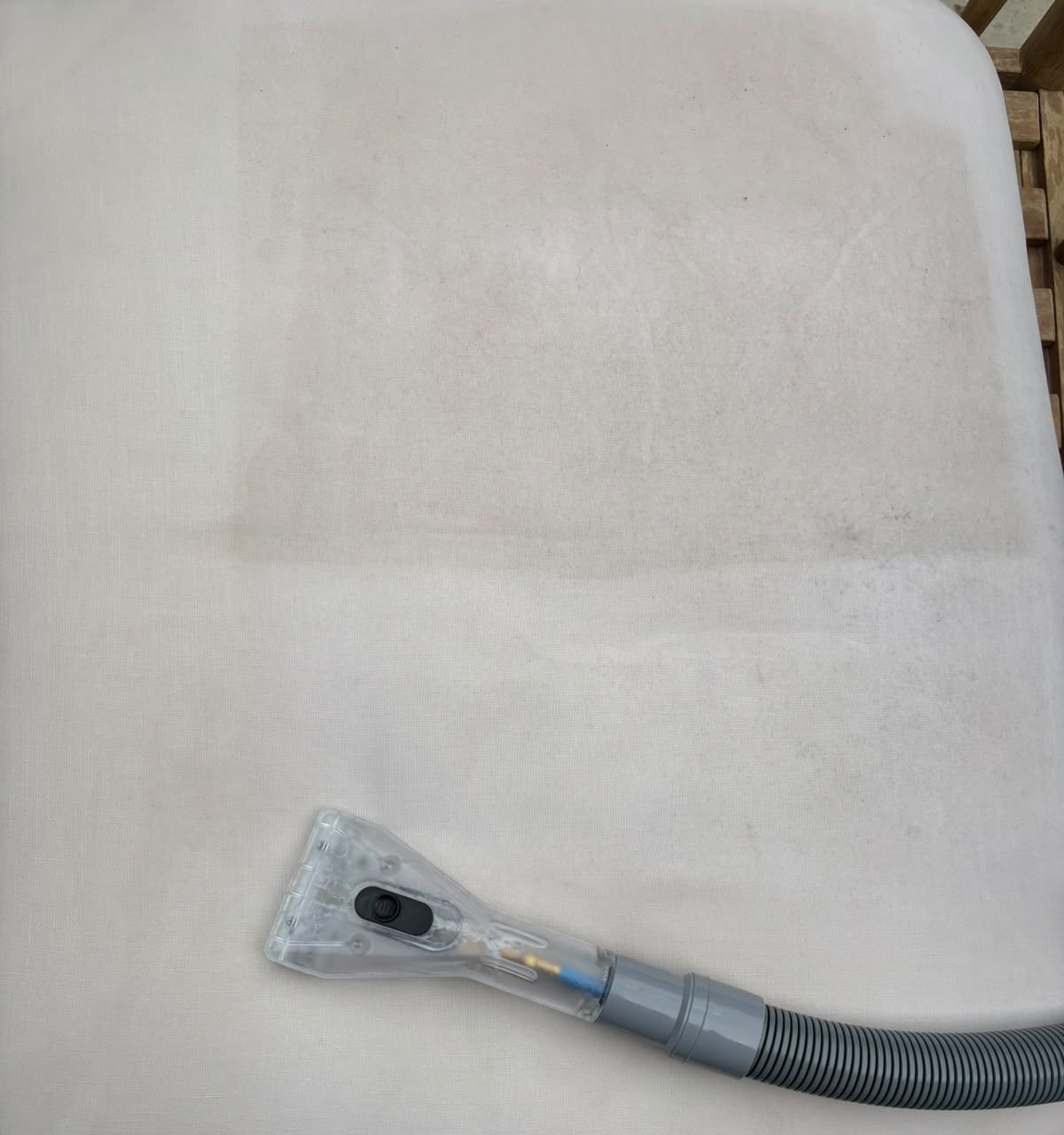 Clear upholstery cleaning tool and hose resting on a cream fabric cushion