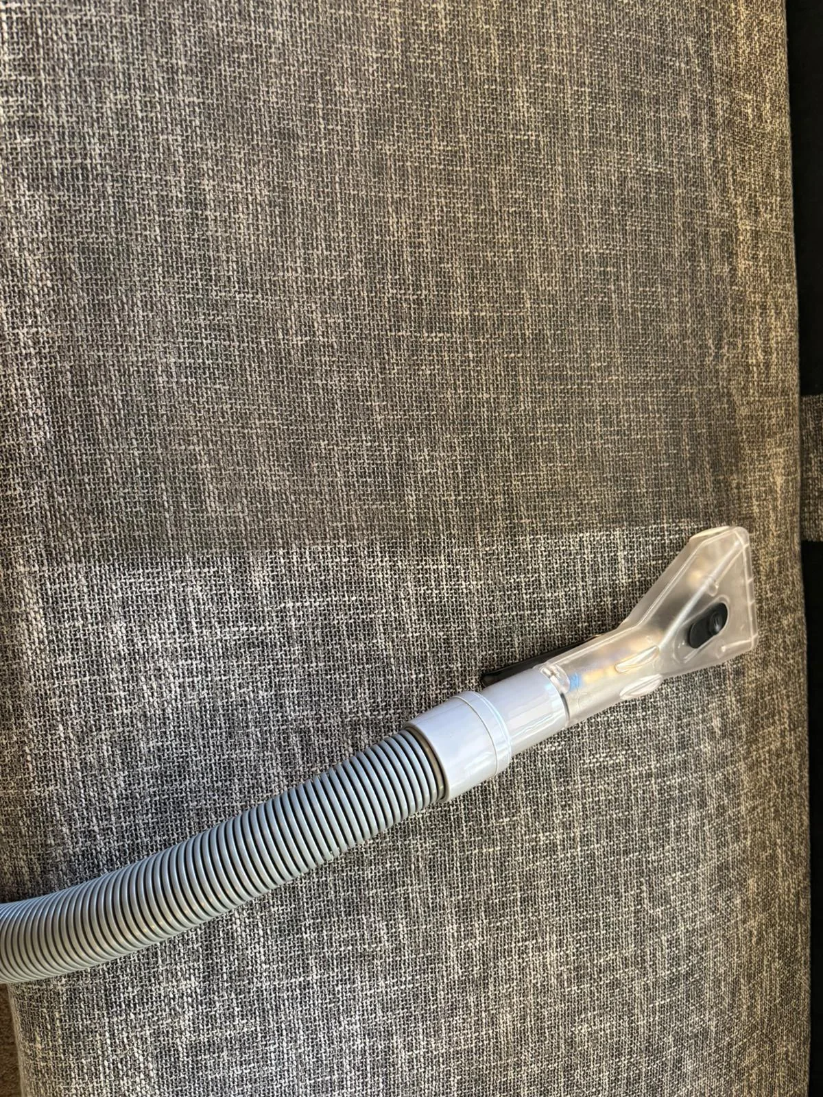 Clear upholstery extraction nozzle cleaning a grey fabric sofa cushion