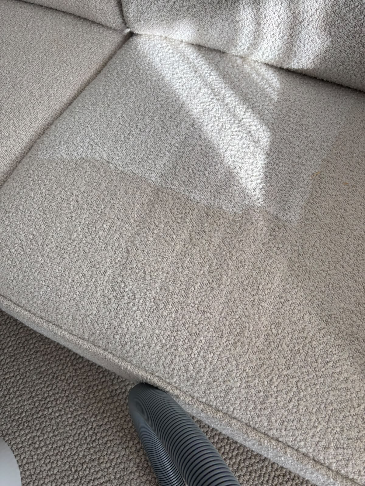 Close-up of a light fabric sofa cushion with an upholstery cleaning hose at its lower edge
